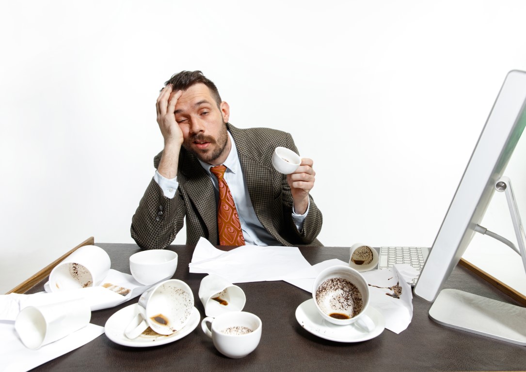 Ein junger Mann trinkt viel Kaffee. Er ist trotzdem nicht in der Lage zu arbeiten, weil er problematische Geschaefte fuert.